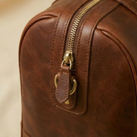 The Voyager full-grain leather duffle — antique brass hardware and zip pull close-up