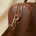 The Voyager full-grain leather duffle — antique brass hardware and zip pull close-up