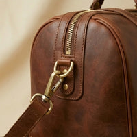The Voyager full-grain leather duffle — antique brass hardware and zip pull close-up