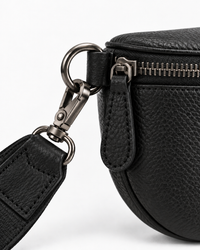 Close-up of the gunmetal-tone clip, zipper and leather strap attachment on the black sling bag.