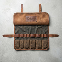 Overhead flat-lay of an empty Elatheria waxed canvas and leather motorcycle tool roll lying flat on a clean, light gray concrete studio background.