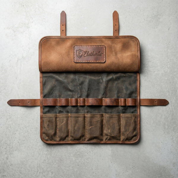 Overhead flat-lay of an empty Elatheria waxed canvas and leather motorcycle tool roll lying flat on a clean, light gray concrete studio background.