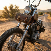 Elatheria leather and waxed canvas tool roll securely strapped to the front forks of a vintage motorcycle under warm golden hour sunlight.