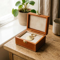 The Keepsake leather memory box open on a windowsill table with brass pet ID tag inside, lifestyle shot