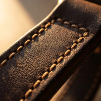 Macro detail of full-grain leather texture and hand-stitching on the dog harness strap