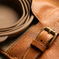 Macro detail of leather grain and brass buckle hardware on The Voyager feeding case