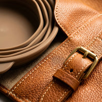 Macro detail of leather grain and brass buckle hardware on The Voyager feeding case