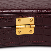 Close-up of the brass hinge and textured burgundy crocodile-embossed leather on the Cadenza violin case