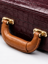 Reinforced tan leather carry handle with brass mounts on the burgundy crocodile-embossed violin case